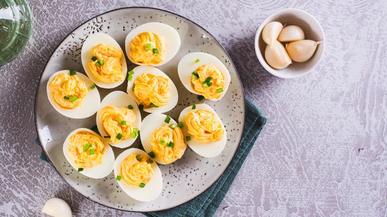 Deviled eggs on a plate next to a ramekin of garlic cloves.