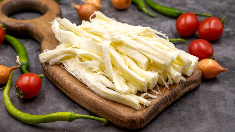 A pile of peeled string cheeses surrounded by tomatoes, shallots, and green peppers