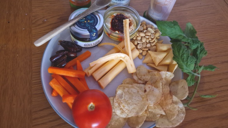 A plate of pickled string cheese surrounded by crackers, peanuts, produce, and dipping sauces