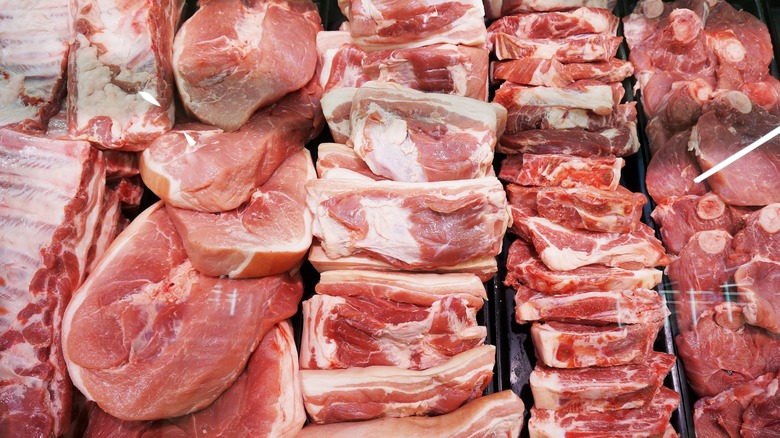 A variety of meats sitting in the cooler of a butcher's counter