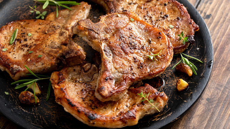 Browned pork chops rest on a black plate