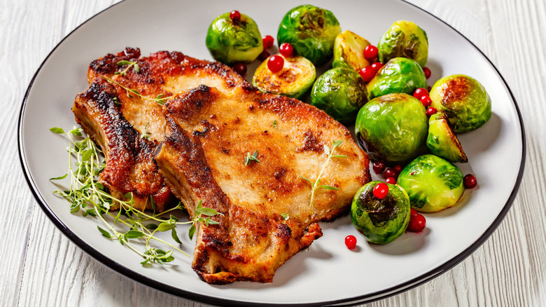 Golden brown bone-in pork chops served with roasted Brussel sprouts