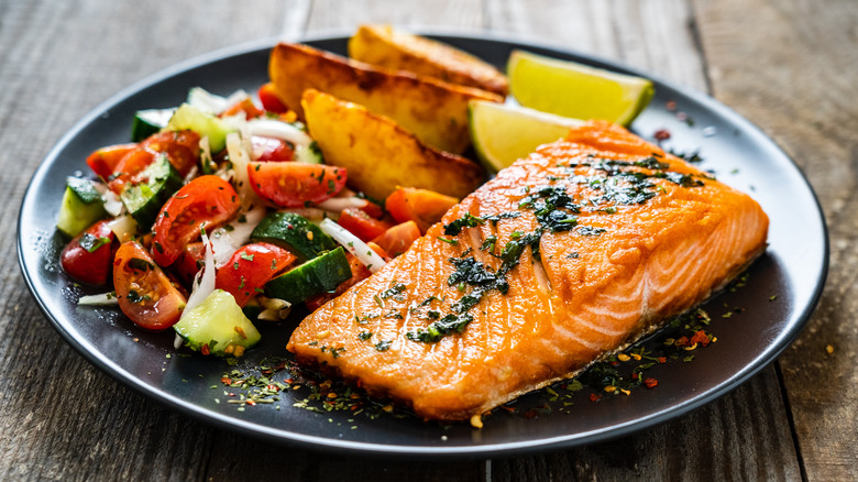 Salmon, veggies, potato wedges on dinner plate