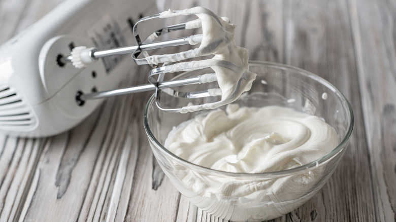 A hand mixer next to a bowl of whipped cream