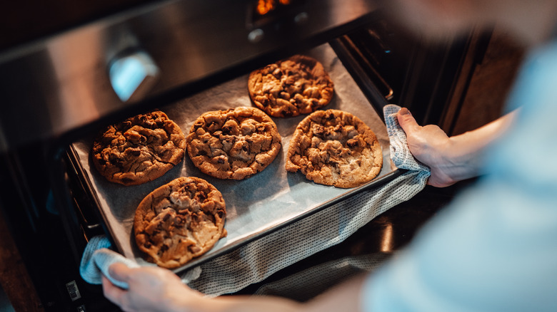 A baker takes a tray of chocolate chip cookies out of the oven