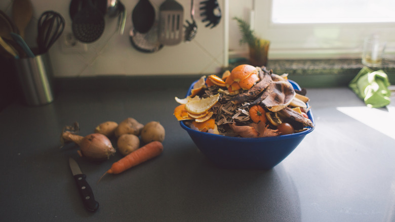 Potatoes, carrot, and onion next to a bowl of discarded scraps