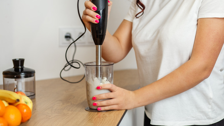 A woman holds an immersion blender in a thick, white mixture