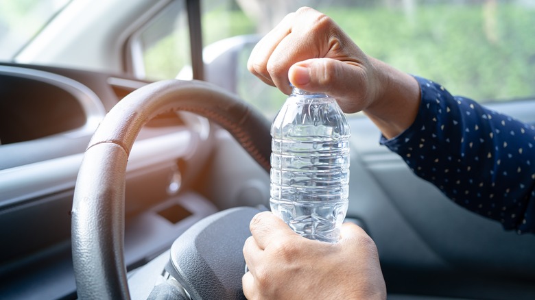 Person opening water bottle in front of steering wheel