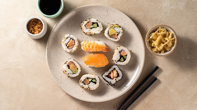 Plate of sushi roll and nigiri pieces next to ginger, soy sauce, and chopsticks