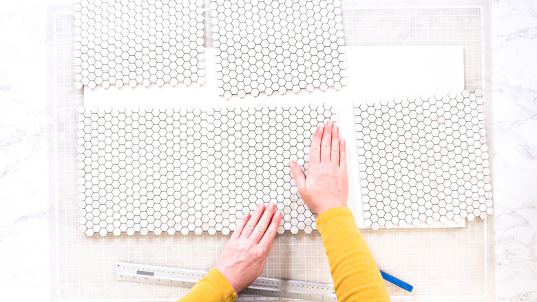 A person measuring a set of peel-and-stick tiles.