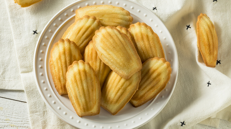 A pile of madeleine cookies sits on a white plate