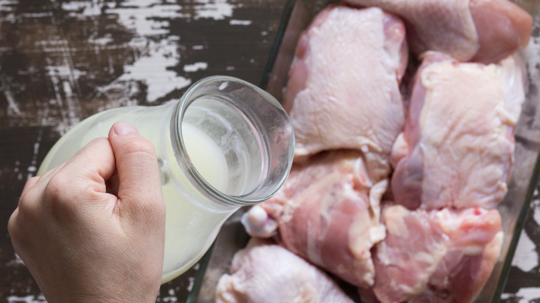 Hands pouring whey over raw chicken