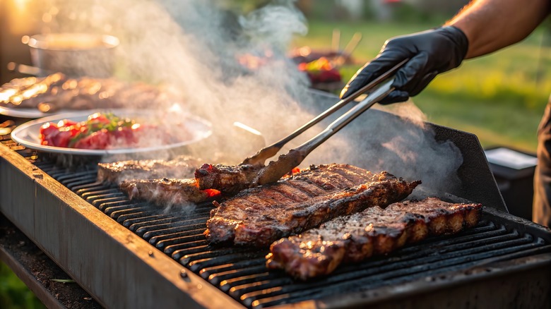 Person using tongs to flip meat that's grilling