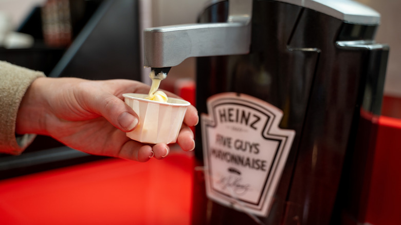 Someone dispensing mayo from a Five Guys mayonnaise canister.