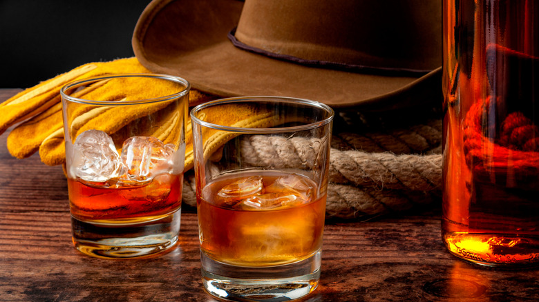 Two glasses of whiskey over the rocks with a cowboy hat behind it.