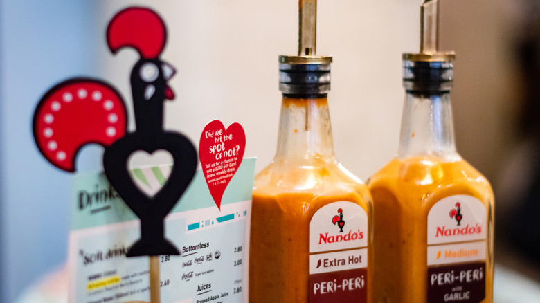 A nando's chicken mascot next to bottles of peri peri sauce