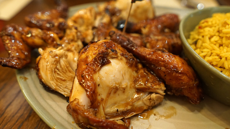 A half roasted chicken covered with peri peri sauce sits next to a side of spiced rice from Nando's