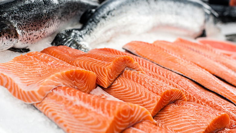 Fresh, brightly-colored salmon fillets sit on ice next to whole fish.