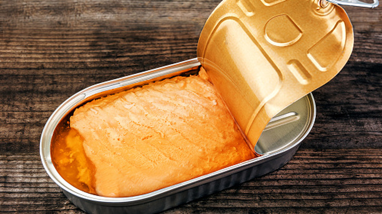 A partially-opened can of salmon sits on a wooden cutting board.