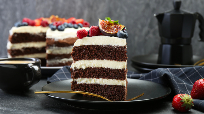 Slice of chocolate cake decorated with fruit on plate with gold fork.