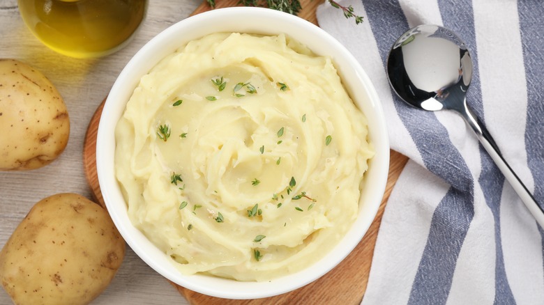 bowl of mashed potatoes next to a whole potato and a spoon and blue and white striped cloth napkin