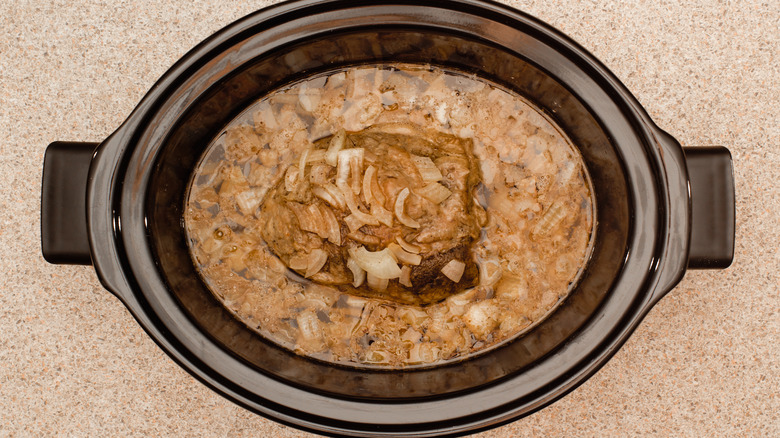Beef, onions, and broth inside a slow cooker