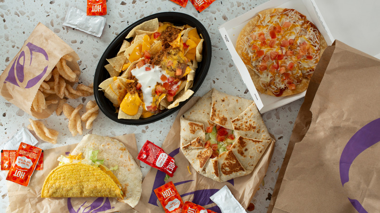 Multiple Taco Bell dishes including nachos, sweets, tacos, and hot sauce packs on table