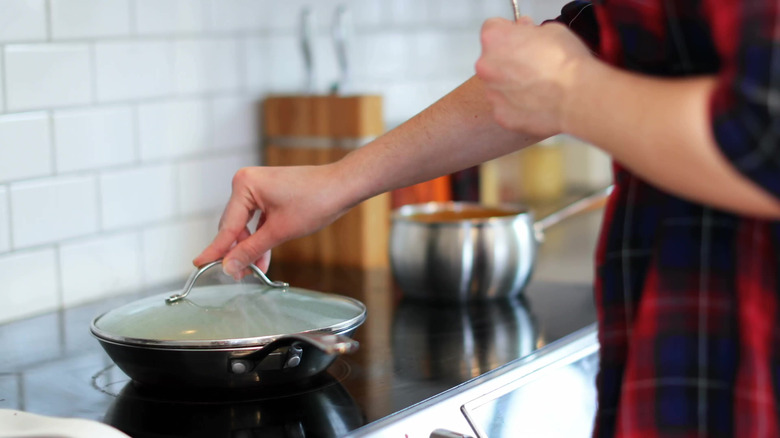 A cook holds a glass lid in place over a hot pan