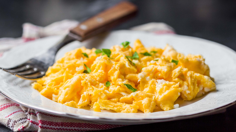 A close-up of a plate of perfectly fluffy scrambled eggs with a fresh herb topping