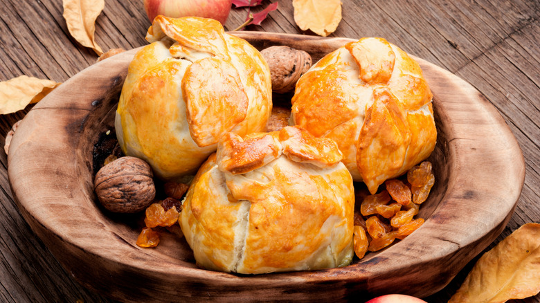 Apple dumplings on a wooden plate surrounded by raisins and walnuts