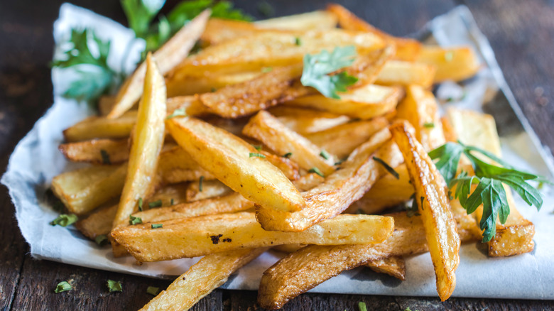 Homemade golden french fries sprinkled with parsley on a white paper on a gray wooden surface