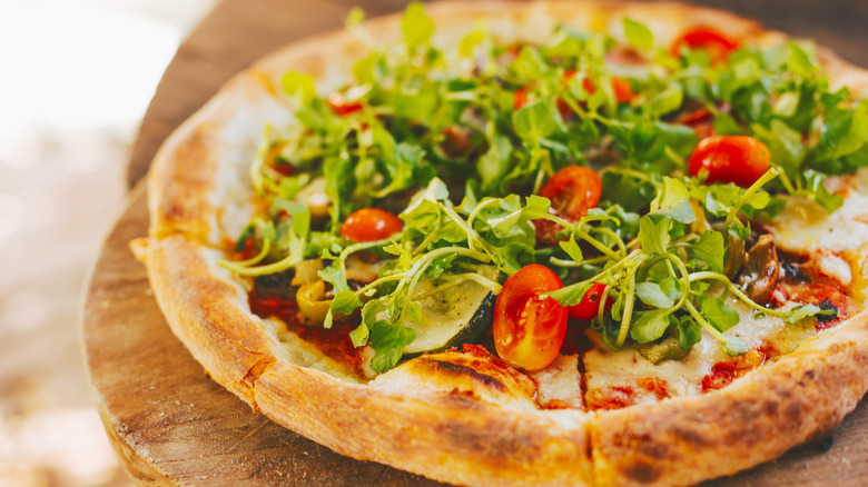 Pizza topped with vegetables, herbs, and cherry tomatoes