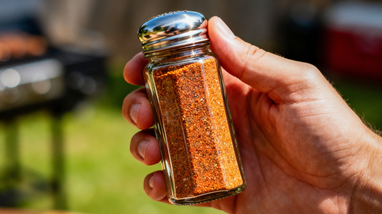 A hand holds a spice jar outside.