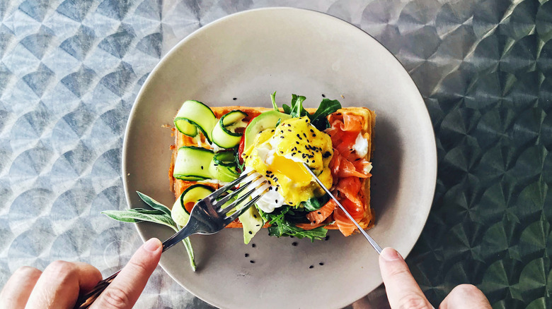 Fork and knife cutting into a poached egg atop an artful breakfast dish