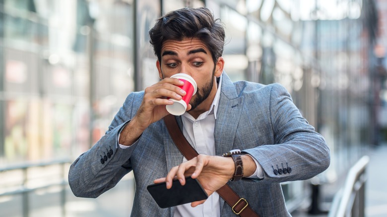 Man in business attire sipping form a travel cup surprised at the time