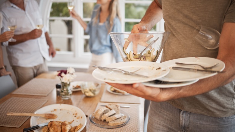 Man gathers used dishes after a meal as others mingle