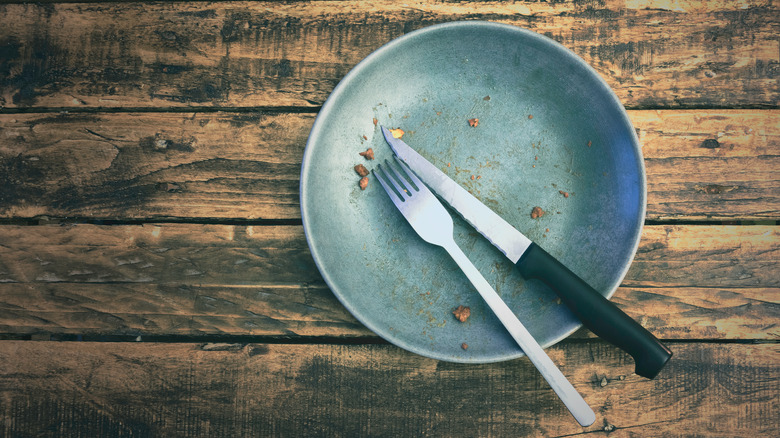 Fork and knife on a dirty blue dish atop a wooden table