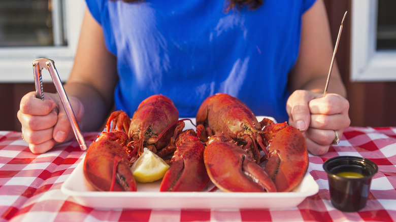 Woman with nutcracker and pick preparing to eat a platter of two lobsters