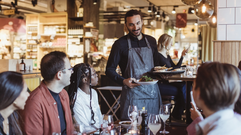 Diners interact with a waiter carrying plates of food