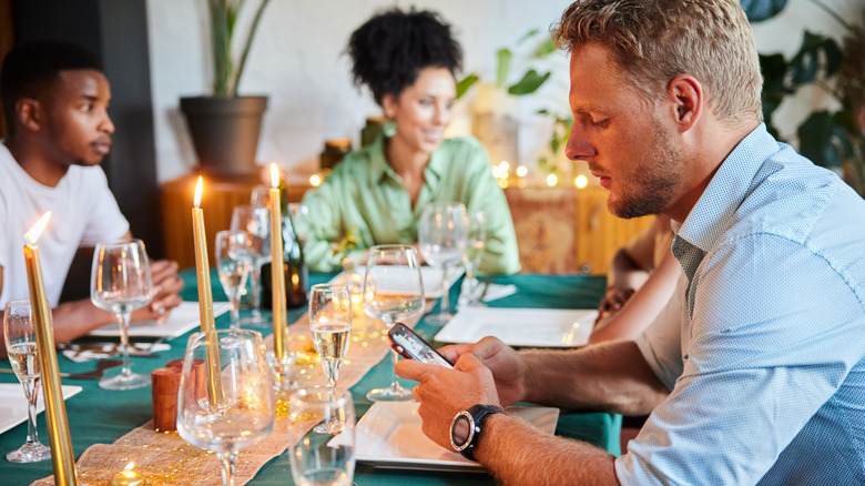 man distracted on cell phone at dinner table