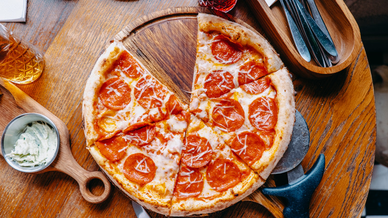 A pizza on a wooden serving board on a table.