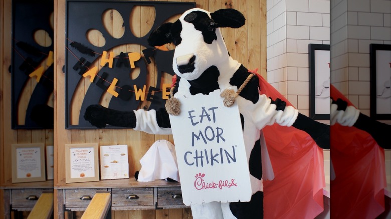 The Chick-fil-A cow mascot wears a sign
