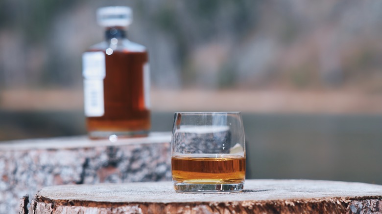 glass of whiskey on wood with bottle in background