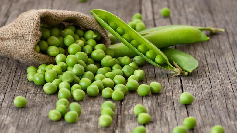 Shelled peas spilling out of a burlap bag on a wood background