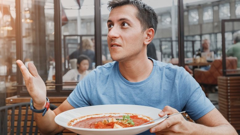 A diner holding a dish of food in a restaurant looks dissatisfied