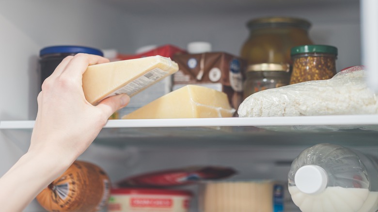 Hand taking cheese from a fridge