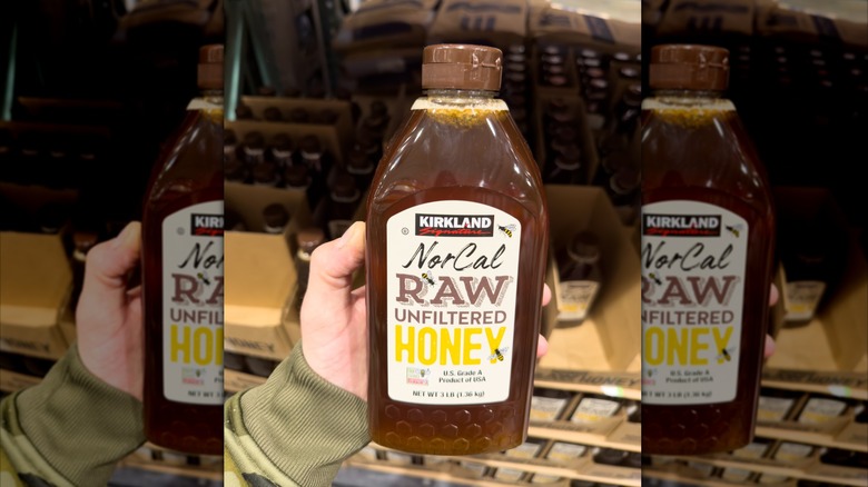 A hand holding a bottle of NorCal raw unfiltered honey.