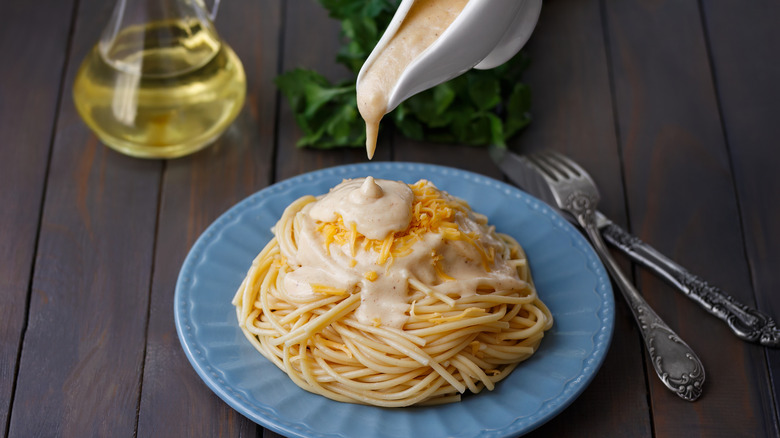 Person pouring bechamel onto cheesy bucatini past