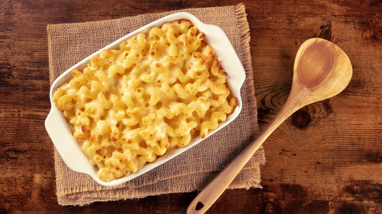 Baked macaroni and cheese in a casserole dish, beside it a wooden spoon