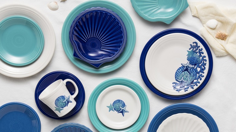 A variety of plates ranging from dark blue to white, with oceanic themes, sit on a table